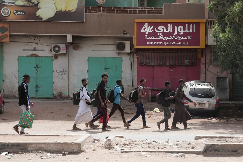 People walk past shuttered shops in Khartoum, Sudan, Monday, April 17, 2023.