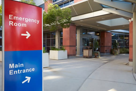 Hospital entrance with sign marking emergency room and main entrance directions.