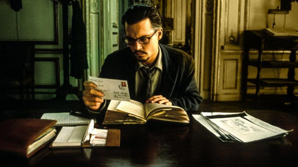 Un hombre con traje se sienta delante de una mesa y lee detenidamente unas cartas.