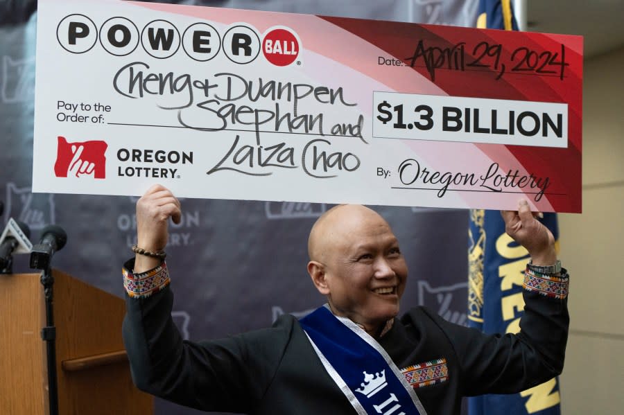 Cheng “Charlie” Saephan holds display check above his head after speaking during a news conference where it was revealed that he was one of the winners of the $1.3 billion Powerball jackpot at the Oregon Lottery headquarters on Monday, April 29, 2024, in Salem, Ore. (AP Photo/Jenny Kane)