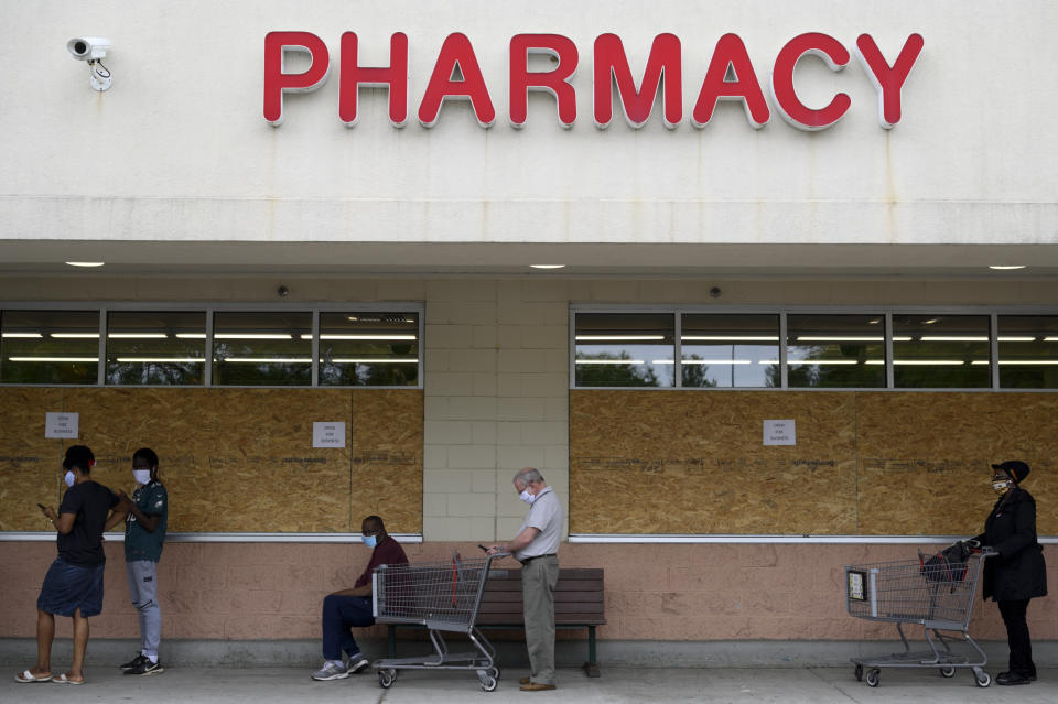 Shoppers wait in line outside a boarded-up grocery store