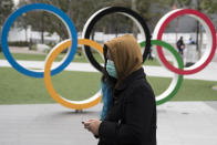 TOKYO, JAPAN - FEBRUARY 26: A woman wearing a face mask walks past the Olympic rings in front of the new National Stadium, the main stadium for the upcoming Tokyo 2020 Olympic and Paralympic Games, on February 26, 2020 in Tokyo, Japan. Concerns that the Tokyo Olympics may be postponed or cancelled are increasing as Japan confirms 862 cases of Coronavirus (COVID-19) and as some professional sporting contests are being called off or rescheduled and some major Japanese corporations ask for people to work from home. (Photo by Tomohiro Ohsumi/Getty Images)