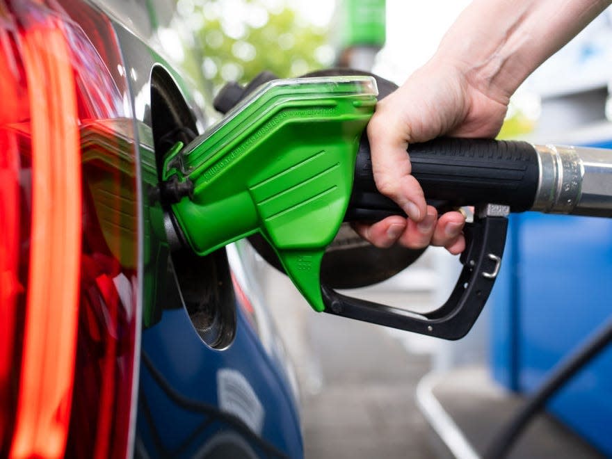 A woman holds a pump nozzle in her hand at a gas station and refuels a car.