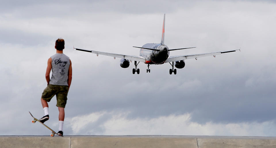 A Jetstar flight takes off as a young boy on a skateboard watches.