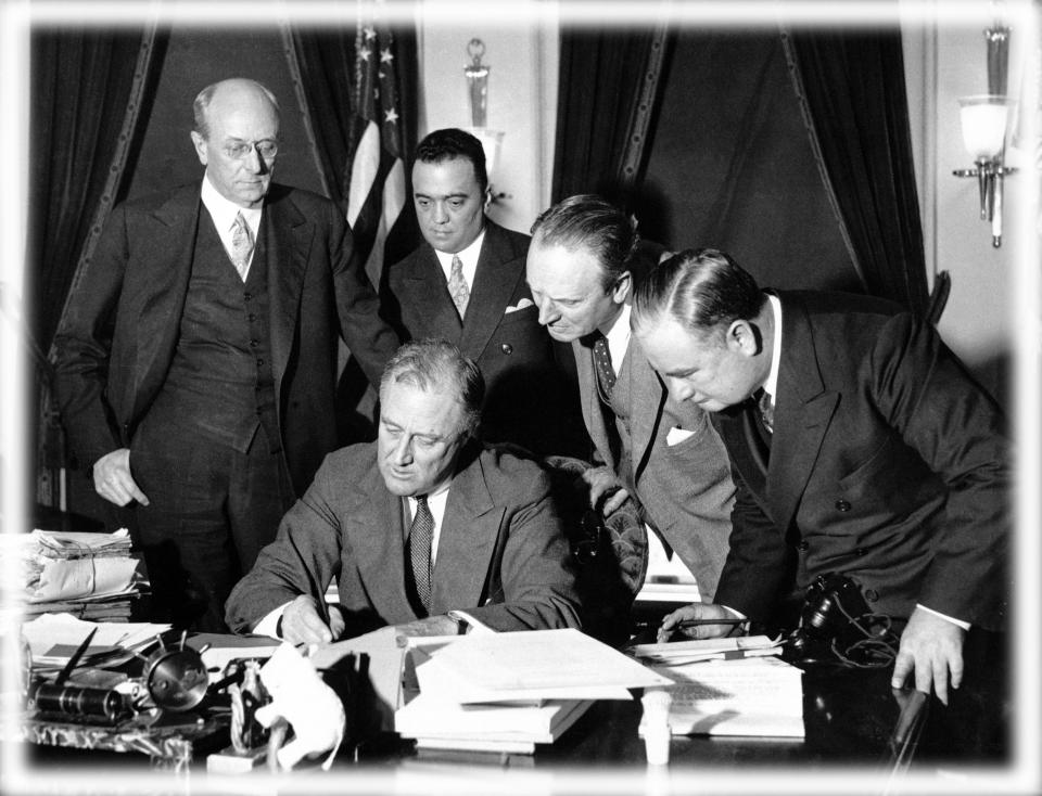 FBI Director J. Edgar Hoover stands behind President Franklin Delano Roosevelt and watches him sign a bill to enforce the fight against crime in 1934. (Photo: Bettmann Archive/Getty Images, digitally enhanced by Yahoo News)
