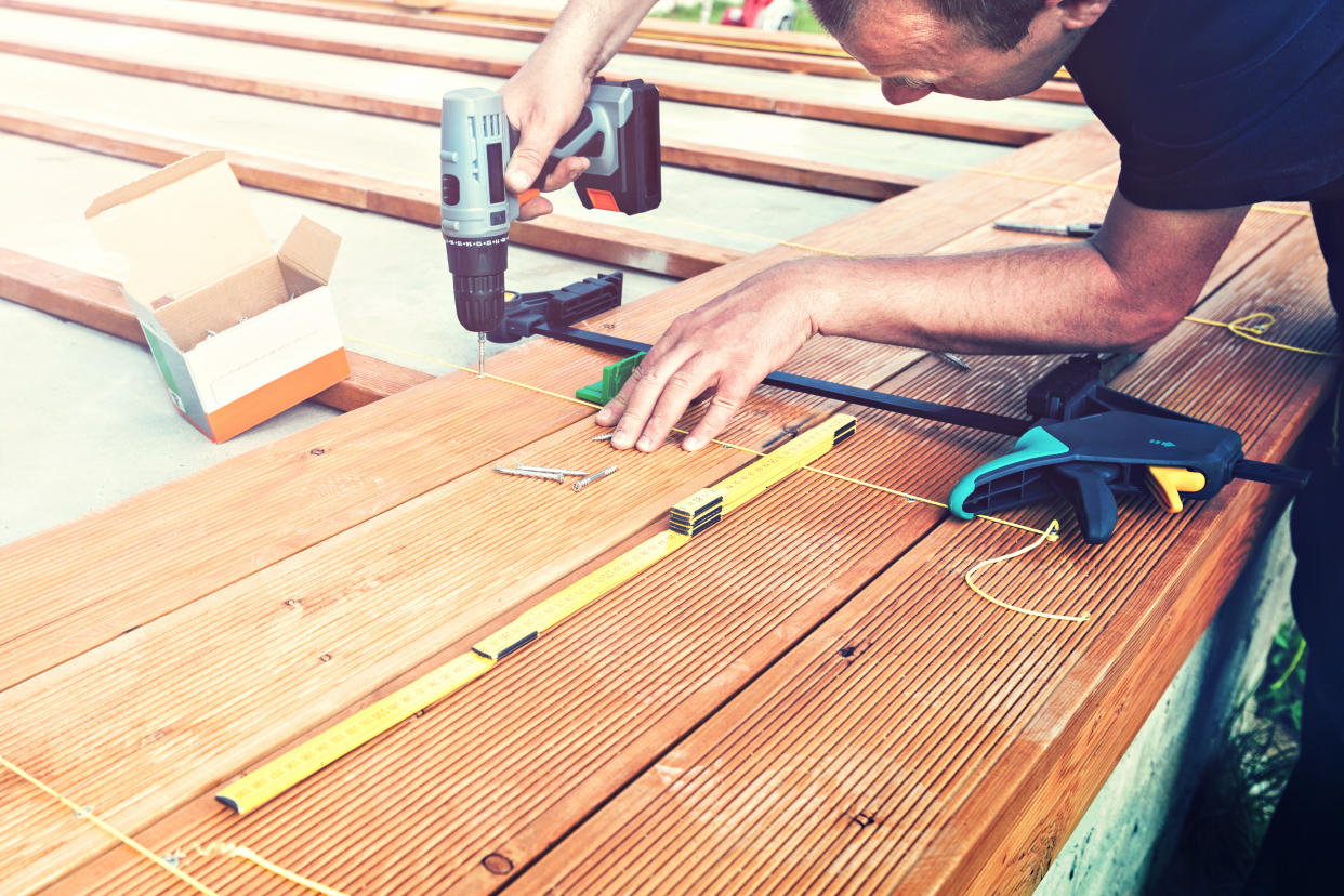 Construction worker screwing down wood deck with battery power screw gun or drill. The man screwed the terrace boards. Carpenter builds a terrace