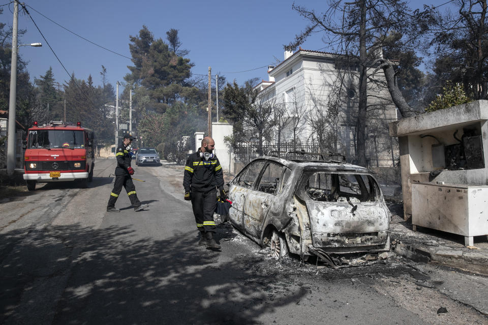 Firefighters look at a burnt car following a forest fire at Dionysos northern suburb of Athens, on Tuesday, July 27, 2021. Greek authorities have evacuated several areas north of Athens as a wildfire swept through a hillside forest and threatened homes despite a large operation mounted by firefighters. (AP Photo/Yorgos Karahalis)