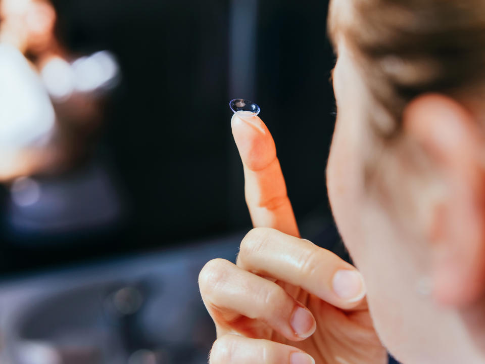 A person is holding a contact lens on the tip of their index finger, preparing to insert it into their eye