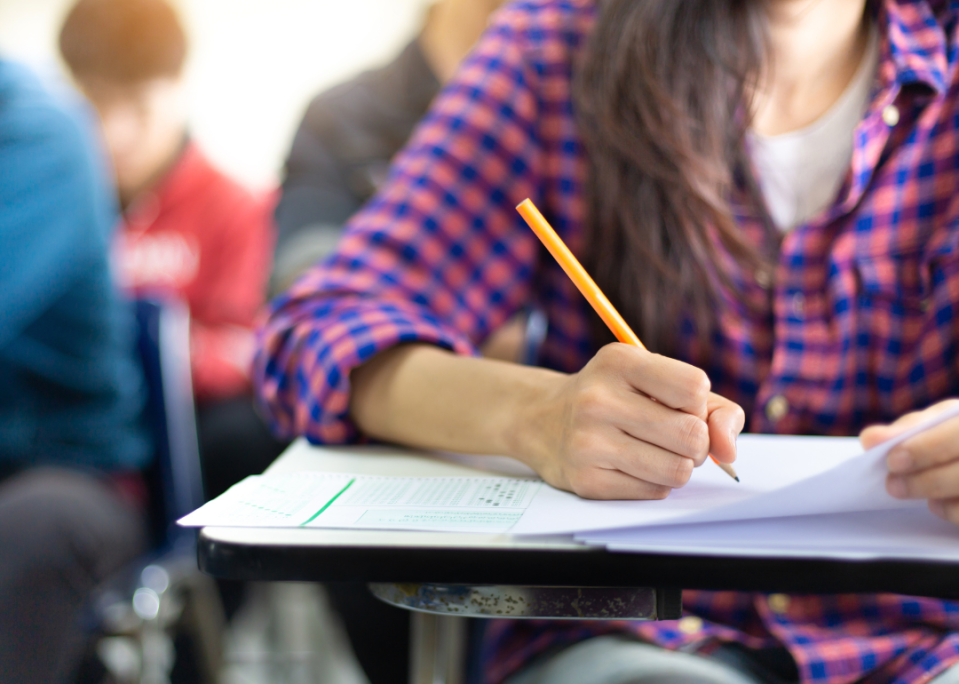 A high school student sitting at a desk writing on a piece of paper.