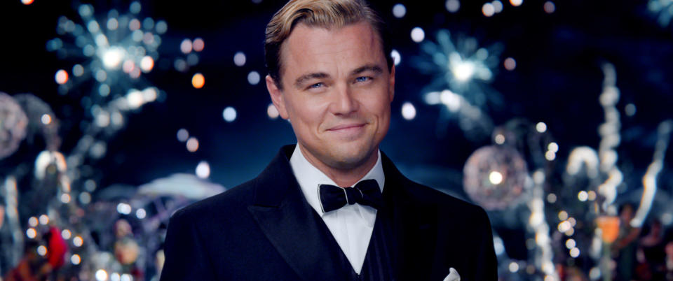 closeup of a man in a suit smiling as fireworks go off behind him