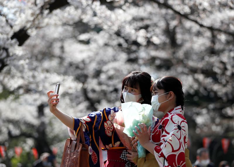 Kimono-clad women wearing protective face masks take selfie photos among blooming cherry blossoms amid the coronavirus disease (COVID-19) pandemic, in Tokyo