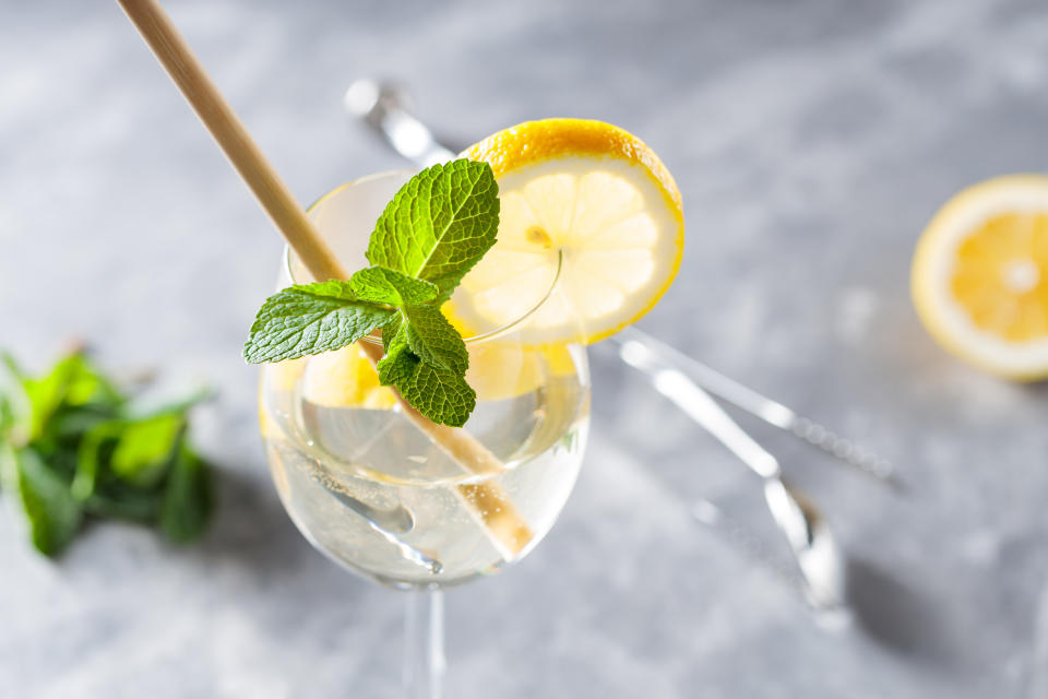 A refreshing Hugo spritz in a stemmed glass garnished with a lemon slice and fresh mint leaves, served with a straw