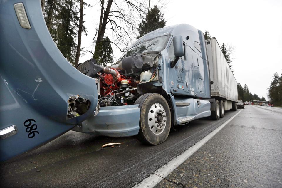 A semi-truck with visible damage to its hood sits parked on the shoulder just ahead of a car covered in mud and debris and with a smashed windshield just beyond where an Amtrak train lay spilled onto Interstate 5 below as some train cars remain on the tracks above, in DuPont, Wash. The Amtrak train making the first-ever run along a faster new route hurtled off the overpass Monday near Tacoma and spilled some of its cars onto the highway below, killing some people, authorities said — Shutterstock/AP