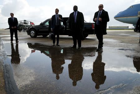 Security personnel are reflected in a puddle while standing before the presidential limo and Air Force One as U.S. President Barack Obama departs Stansted Airport in Stansted, Britain April 24, 2016. REUTERS/Kevin Lamarque