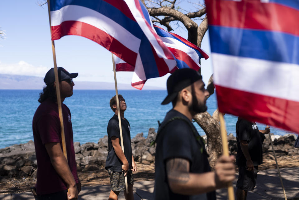 Lahaina, Hawaii, residents, who are affected by a deadly wildfire that devastated the community, hold Hawaiian flags a news conference in Lahaina, Hawaii, Friday, Aug. 18, 2023. (AP Photo/Jae C. Hong)