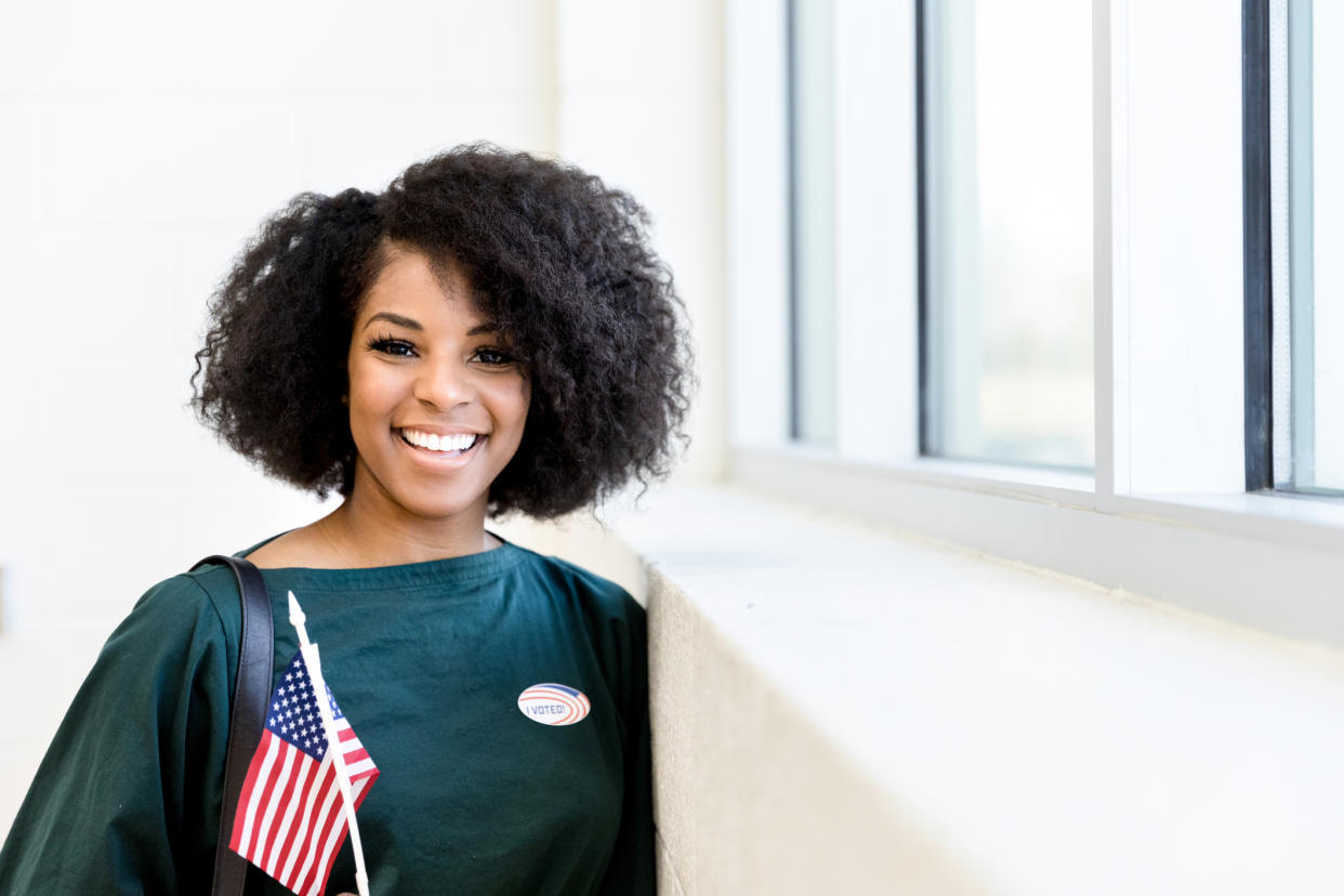 Mid adult woman holding American flag and 'I voted' sticker smiling for camera.