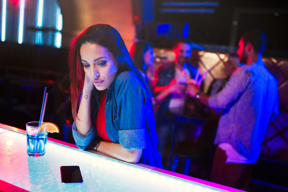 Woman leaning on bar with a drink, looking upset