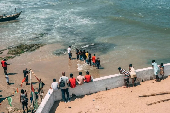 A group of African-American tourists hold hands as they enter the ocean in a remembrance ceremony after visiting the “Door of No Return” at the Cape Coast Castle on Aug. 18, 2019. (Photo by Natalija Gormalova/AFP via Getty Images)