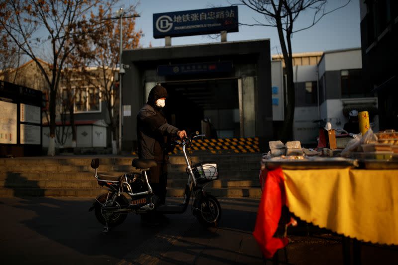 A man wearing a face mask stands next to his scooter outside a subway station as the country is hit by an outbreak of the new coronavirus, in Beijing