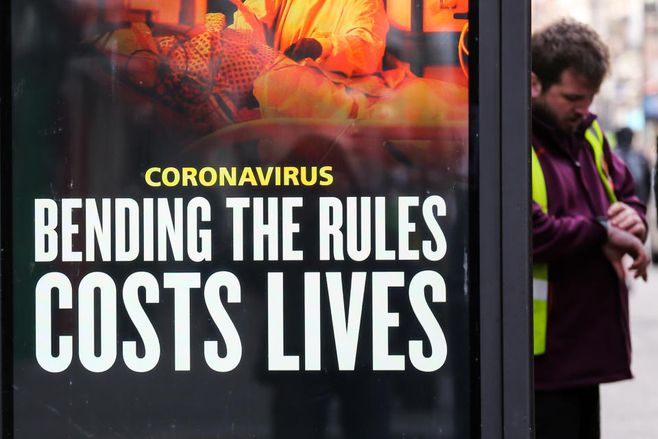 LONDON, UNITED KINGDOM - 2021/01/22: A man looks at his watch while standing next to a covid-19 prevention publicity campaign poster in London. According to the Office for National Statistics (ONS) as of January 15 there had been over 103,000 Covid-19 deaths in the UK. (Photo by Dinendra Haria/SOPA Images/LightRocket via Getty Images)