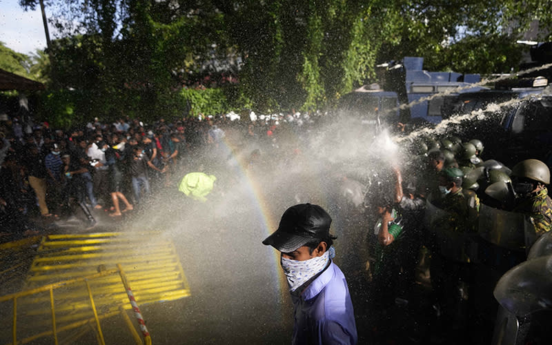 Police fire tear gas and water cannons, one of which causes a rainbow to form near dispersing protest members