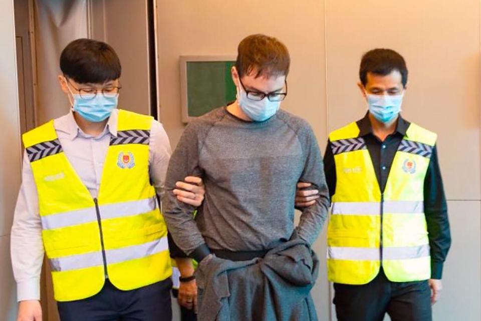 David James Roach being escorted by police officers after arriving in Singapore on 17 March 2020. (PHOTO: Singapore Police Force) 