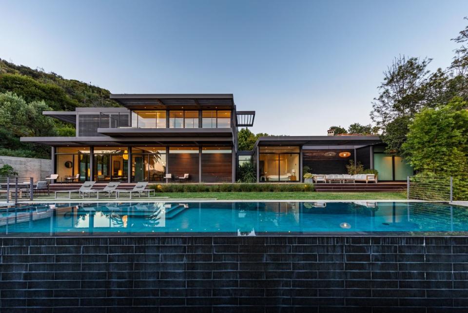 The back of the home has walls of glass; a large rectangular pool runs the length of the home.