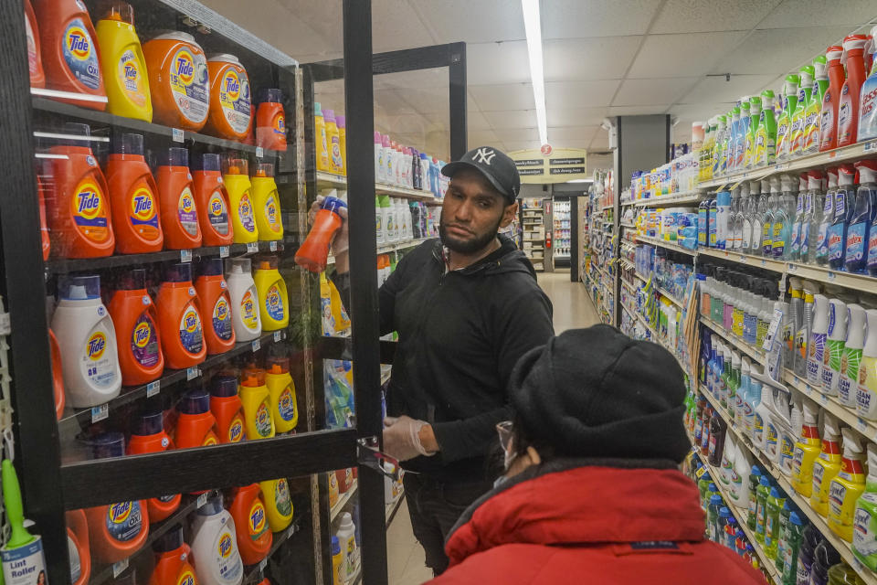 Leo Pichardo, left, a store associate at Gristedes supermarket, retrieves a container of Tide laundry soap from a locked cabinet, Tuesday Jan. 31, 2023, at the store in New York. Increasingly, retailers are locking up more products or increasing the number of security guards at their stores to curtail theft. (AP Photo/Bebeto Matthews)