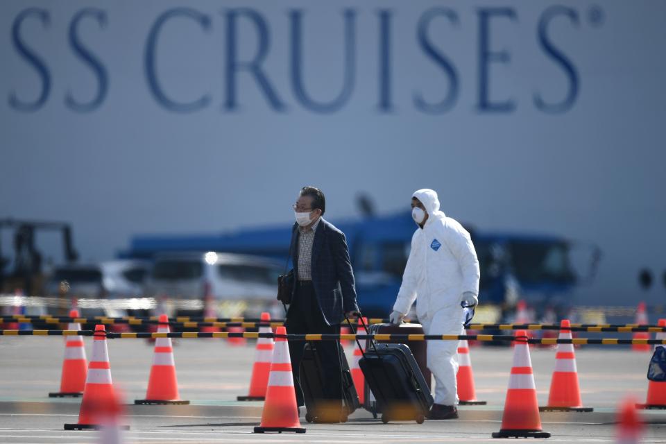 A passenger (L) disembarks from the Diamond Princess cruise ship - in quarantine due to fears of the new COVID-19 coronavirus - at the Daikoku Pier Cruise Terminal in Yokohama on February 19, 2020.