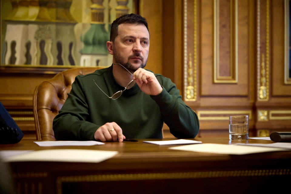 Ukraines Präsident Wolodymyr Selenskyj sitzt an einem Tisch im Büro und hält eine Brille in der Hand