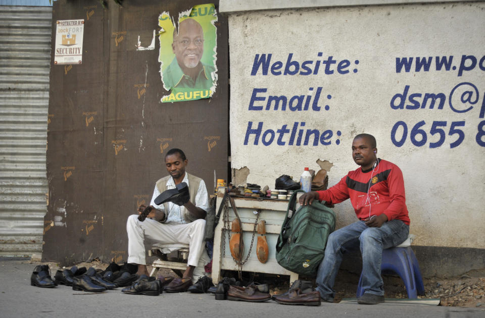 FILE - In this Tuesday, Oct. 27, 2015 file photo, a Tanzanian shoe-shiner conducts his business underneath an election poster for then ruling party presidential candidate John Magufuli, in Dar es Salaam, Tanzania. President John Magufuli of Tanzania, a prominent COVID-19 skeptic whose populist rule often cast his country in a harsh international spotlight, has died aged 61 of heart failure, it was announced Wednesday, March 17, 2021 by Vice President Samia Suluhu. (AP Photo/Khalfan Said, File)