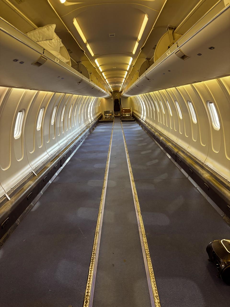 Interior view of an empty airplane fuselage without seats, showing overhead bins and cabin lighting