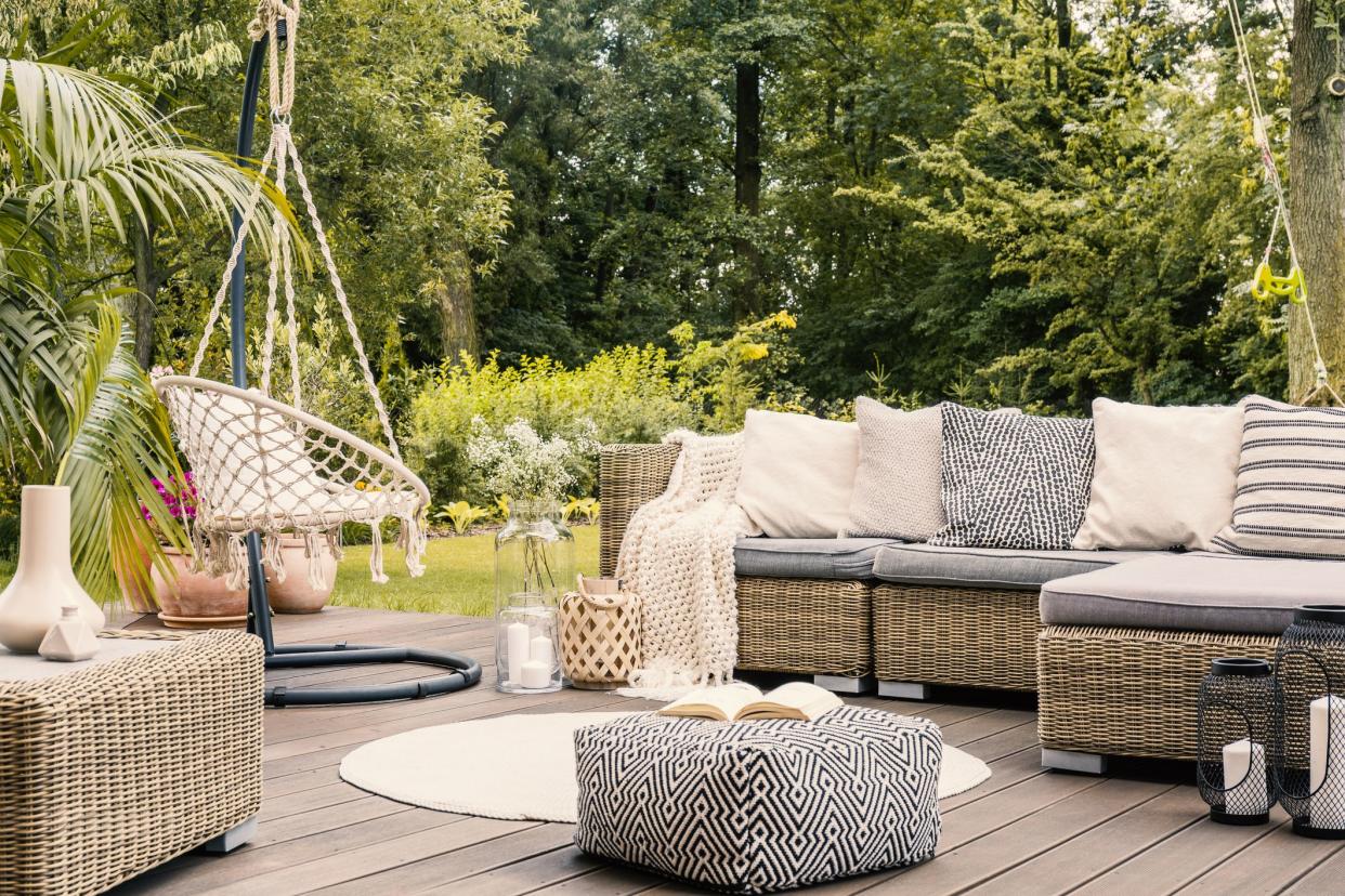 Book on a black and white pouf in the middle of a bright terrace with a rattan corner sofa, hanging chair and round rug. Real photo