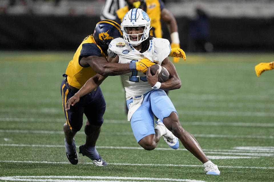 North Carolina quarterback Conner Harrell is tackled by West Virginia linebacker Lee Kpogba during the first half of an NCAA college football game at the Duke's Mayo Bowl Wednesday, Dec. 27, 2023, in Charlotte, N.C. (AP Photo/Chris Carlson)