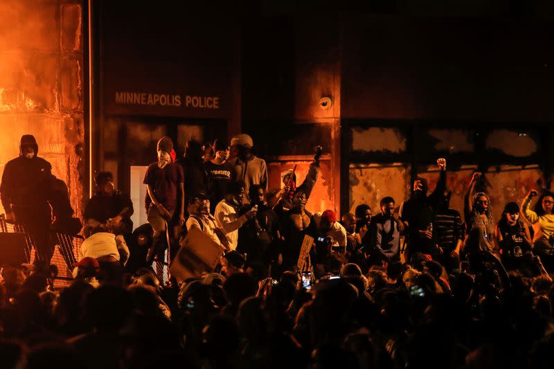 Protesters gather around after setting fire to the entrance of a police station as demonstrations continue in Minneapolis