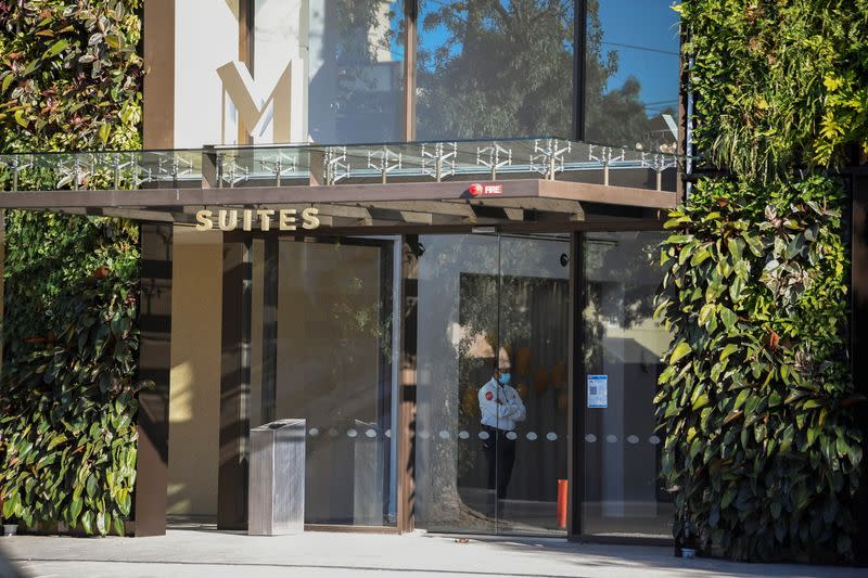 A security staff member wearing a protective face mask stands inside the door of the M Suites hotel where tennis players are undergoing quarantine in Adelaide