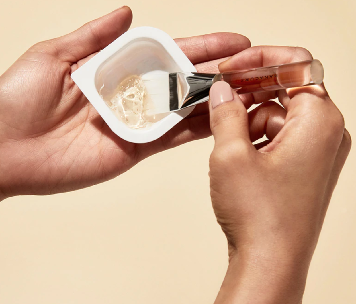 Hands using a brush to mix beauty product.