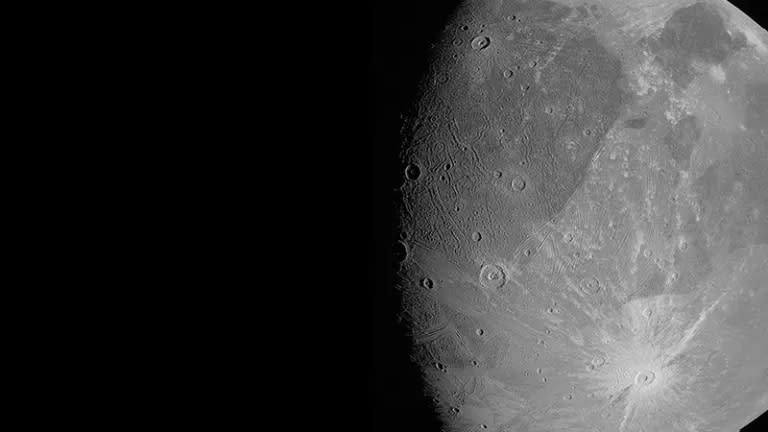 a rocky moon on the right of the image has lots of craters spread across the surface.