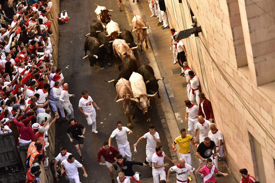 People run through the street with fighting bulls at the San Fermin Festival in Pamplona, northern Spain, Friday, July 8, 2022. Revellers from around the world flock to the city every year for nine days of uninterrupted partying in Pamplona's famed running of the bulls festival which was suspended for the past two years due to the coronavirus pandemic. (AP Photo/Alvaro Barrientos)