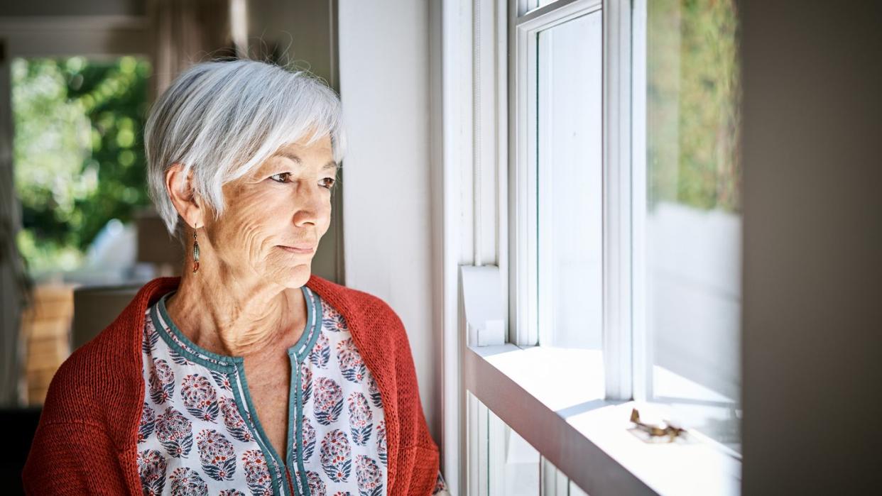 senior woman standing alone by a window at home