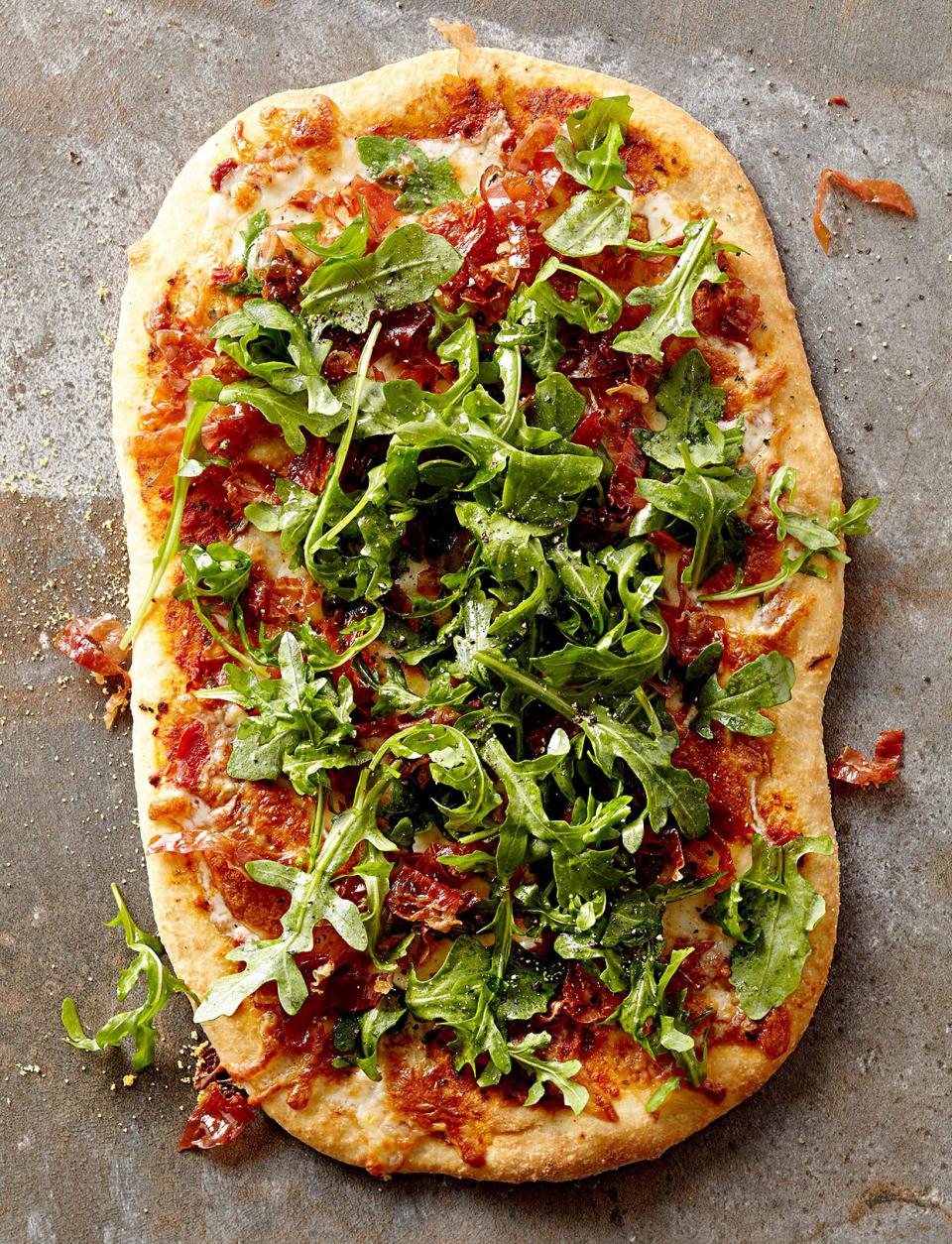 The flatbread recipe is full of Mediterranean flavor thanks to tomato pesto, prosciutto, provolone cheese, and peppery arugula.