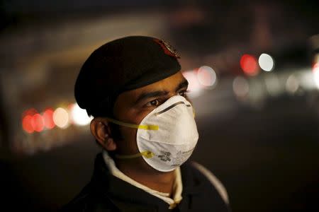 A traffic policeman wears a mask to protect himself from dust and air pollution as he stands on a road-divider in New Delhi, India, December 23, 2015. To match INDIA-POLLUTION/ REUTERS/Adnan Abidi