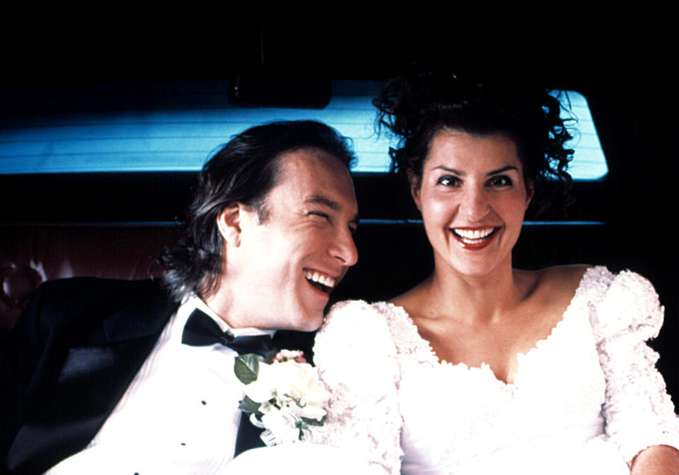 John Corbett and Nia Vardalos from "My Big Fat Greek Wedding" smiling in groom and bride outfits in a car