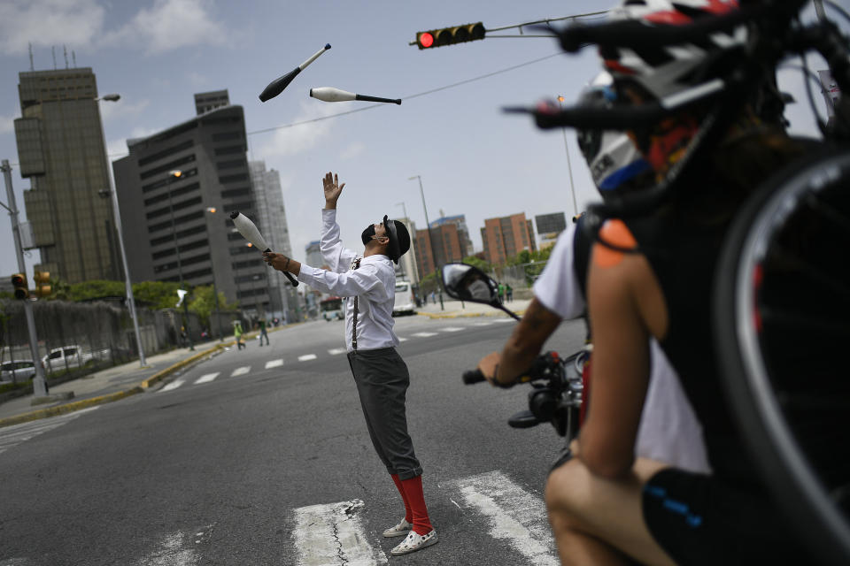 A street juggler wearing a protective face mask, performs at a street crossing during a red light in Caracas, Venezuela, Saturday, July 11, 2020, amid a government-ordered lockdown to curb the spread of the new coronavirus.(AP Photo/Matias Delacroix)