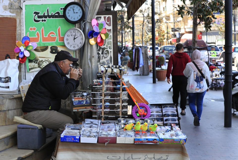 Salah Nasab, a Lebanese street vendor who also sells and repairs clocks, sits next to two clocks that show different times in the southern port city of Sidon, Lebanon, March 27, 2023. / Credit: Mohammad Zaatari/AP