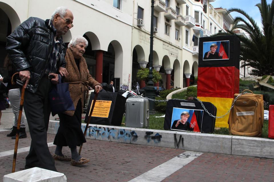 An elderly couple walk past a portrait of German Chancellor Angela Merkel, set up by protesters to use as a dart board, in the northern Greek city of Thessaloniki on Friday, April 11, 2014. Merkel was paying a brief visit to Athens a day after the crisis-hit country returned to international bond markets. Police banned protests across most of central Athens, and deployed some 5,000 officers across the capital. (AP Photo/Nikolas Giakoumidis)