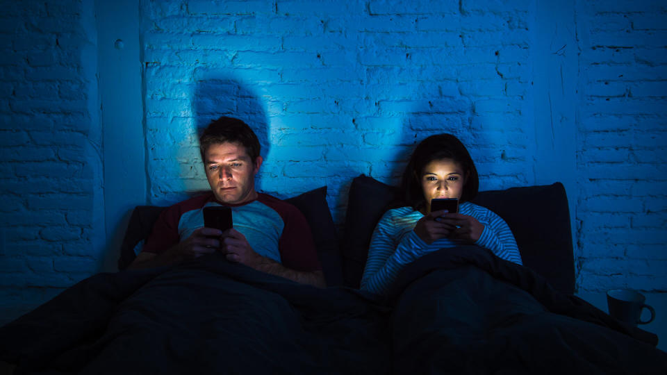 young couple at home in bed late at night using mobile phone in relationship communication problem and internet social media network concept.