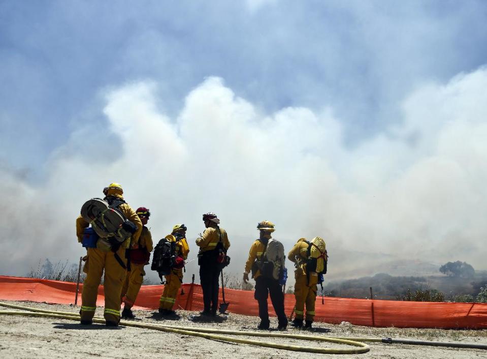 Firefighters face a huge smoke cloud as they plan their attack on a wild fire Tuesday, May 13, 2014, in San Diego. Wildfires destroyed a home and forced the evacuation of several others Tuesday in California as a high-pressure system brought unseasonable heat and gusty winds to a parched state that should be in the middle of its rainy season. (AP Photo)