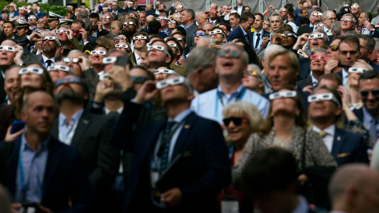 Sea-Air-Space attendees step out of the naval conference in National Harbor, Maryland, to observe the solar eclipse April 8, 2024. (Colin Demarest/C4ISRNET)