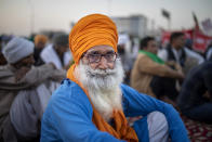 FILE- In this Dec. 9, 2020 file photo, an elderly farmer listens to a speaker as farmers protesting against new farm laws block a major highway at the Delhi-Uttar Pradesh state border, India. India is expanding its COVID-19 vaccination drive beyond health care and front-line workers, offering the shots to older people and those with medical conditions that put them at risk.(AP Photo/Altaf Qadri, File)